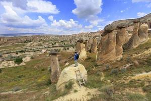 A young man stands on a rock and looks at the opening landscape and blue sky in Cappadocia.