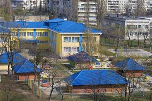 Bright blue roof of kindergarten against the background of gray urban high-rise buildings photo