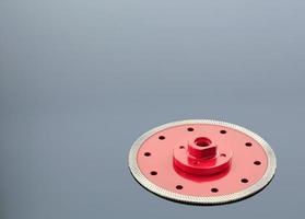 Diamond cutting wheel is red with a threaded nut on the mirror surface of a gray background with a slight gradient photo