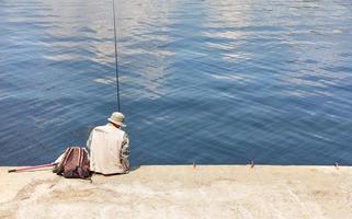 un pescador solitario se sienta en un muelle de hormigón con una caña de pescar cerca del agua en un día soleado de verano. foto