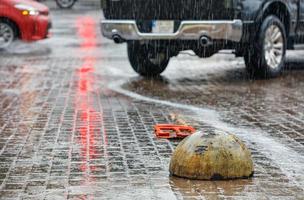 fuertes lluvias caen por el hemisferio de estacionamiento de concreto en la acera y los autos en la intersección. foto