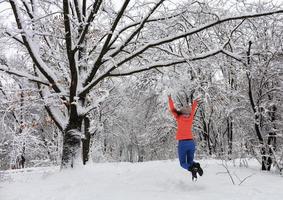 Young beautiful girl walks and happily jumps in the winter in the snow-covered fairy-tale forest near the branchy perennial old oak photo