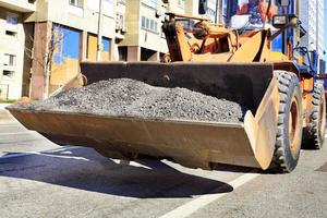 La topadora de construcción pesada lleva en la cuchara el asfalto viejo durante la reparación de la calzada. foto