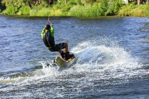 un wakeboarder corre a través del agua a gran velocidad a lo largo de la verde orilla del río. foto