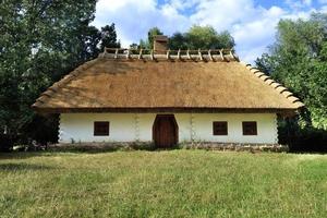 Old traditional Ukrainian rural house with thatched roof and wicker fence in the garden photo