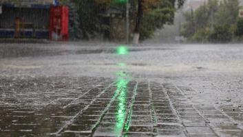 Heavy rain on the sidewalk and asphalt road is illuminated by a green traffic light. photo