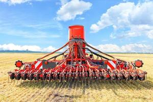 Una grada agrícola multifuncional se encuentra en un campo de trigo cosechado contra un cielo nublado azul en un día de verano. foto