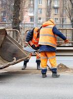 The road workers shovel the dirty sand accumulated between the lanes of the road into the grader's bucket. Vertical image. photo