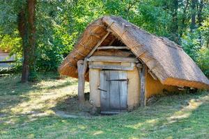 una antigua bodega de barro con techo de paja en el jardín de verano de una finca rural. foto