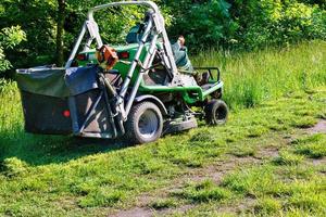 A professional tractor mower driven by a public utility worker climbs up the slope and mows tall grass. photo