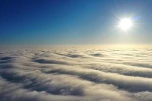 Aerial photography, bright sun above the horizon and above dense gray clouds in a dark blue sky.