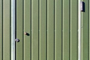 Green metal fence and doors made of corrugated steel sheet with vertical rails and a surveillance camera. photo