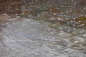 Los círculos concéntricos durante la lluvia en la superficie del agua cubren el área de granito de la acera de la ciudad. foto