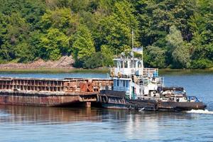 An old river tug pushes an empty barge ahead of itself along the river bank. photo