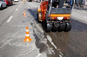 Heavy orange vibratory road roller compacts asphalt on the repaired part of the city road. photo