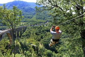 A tourist crosses over a long cable car over a mountain and a forest across the Tiara River. photo