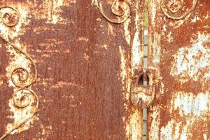 An old rusty lock connects a rusty gate. Rust on old metal sheet texture. photo