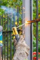 A welder works with metal, welds a metal fence in a park area.