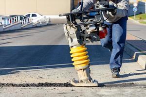 A road worker operates a vibratory rammer to fill the road with asphalt.