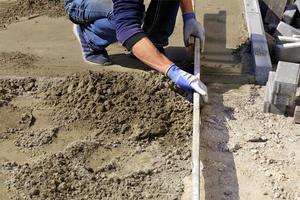 Worker aligns the foundation with a wooden plank for laying tiles on the sidewalk. photo