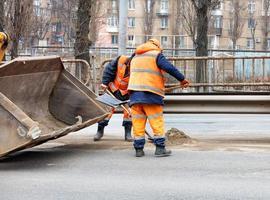 los trabajadores de la carretera usan palas para raspar la arena acumulada entre los carriles de la carretera y cargarla en el balde nivelador. foto
