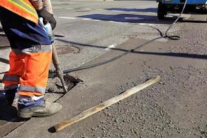 A worker clears a piece of asphalt with a pneumatic jackhammer in road construction. photo