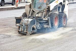 Compact road tractor with hydraulic attachment cuts cracks when repairing road foundations.