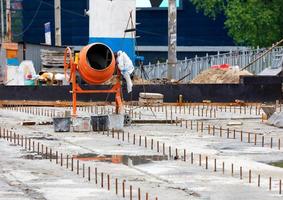 A large orange mortar mixer stands against the backdrop of a road repair work area. Copy space. photo