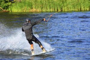 un wakeboarder corre a través del agua a gran velocidad a lo largo de la verde orilla del río.