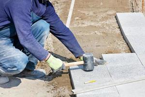 A worker places granite blocks on the sidewalk with a rubber hammer on a marked area. photo