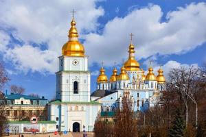 The famous Mikhailivsky Golden-Domed Cathedral and the bell tower in Kyiv in early spring against a blue cloudy sky.