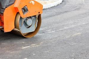 The wheel of a large road vibratory roller compacts fresh asphalt of the new road. photo