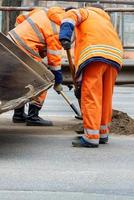 A team of road workers use shovels to clean a section of the road. Vertical image. photo