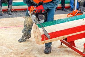 Man holds a chainsaw in his hands and cuts a marked log for accuracy on competition of lumberjacks. photo