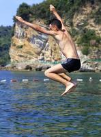 Brave teen jump in the sea against the backdrop of rocks and shoreline photo