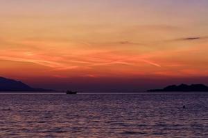 Silhouette of a sea boat running along the horizon of the sea line against the backdrop of a beautiful, vibrant sunset on the Gulf of Corinth. photo