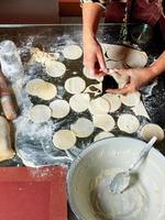 A woman using a rolling pin and a glass prepares a dough for making dumplings. photo