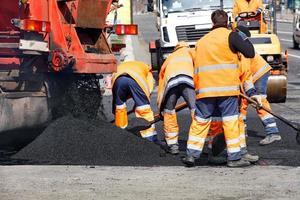 el equipo de trabajo esparce una parte del asfalto con palas para reparar un tramo de la vía. foto