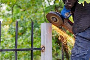 A worker uses a disc angle grinder to trim a metal post. photo
