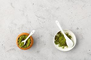 Matcha green tea powder in oak cup with white ceramic spoon and in ceramic cup with white ceramic spoon. photo