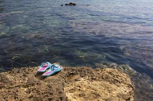 zapatillas de playa se encuentran en una piedra cerca del mar transparente foto