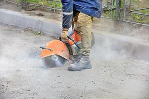 Un trabajador de la construcción que usa una sierra de gasolina portátil corta asfalto viejo para reparar un sitio en la carretera. foto