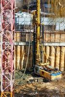 A heavy excavator, together with a drilling rig, is working at a construction site to strengthen the foundation of a future high-rise. Vertical image. photo