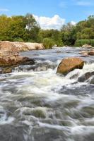 Tormentosos arroyos de agua bañan las rocosas orillas del río, superando los rápidos en un brillante día de verano, imagen vertical. foto