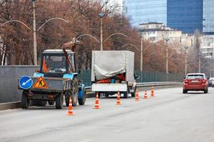 A team of road service workers on an old communal tractor and a truck are enclosing a section of the road with orange cones for subsequent cleaning. photo