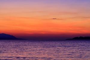 hermosa y brillante puesta de sol en el golfo de corinto contra el fondo de la silueta de las tierras altas que se extienden a lo largo del horizonte de la línea del mar. foto