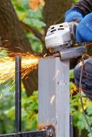 The hands of the worker cut and level the metal post with an angle grinder, hot sparks fly out during the metal cutting. photo