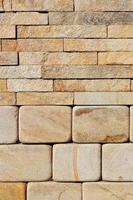 A stack of hewn, rounded yellow sandstone stones in the lower half and rough rectangular tiles at the top.