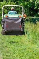A gardener mows tall green grass and collects it in the hopper of a professional lawn mower. The background is slightly blurred. photo