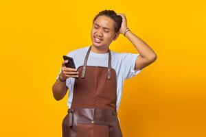 Portrait of handsome asian man holding smartphone touching his head and expressing concern on yellow background photo
